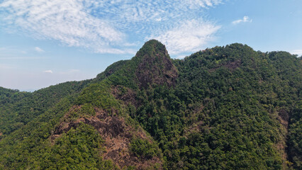 Majestic mountain peak, covered in lush green vegetation, rises towards a vibrant blue sky dotted with wispy white clouds, creating a breathtaking natural landscape