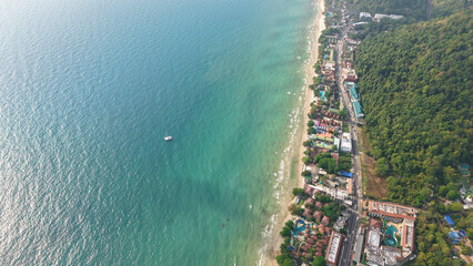 Breathtaking aerial perspective captures the harmonious meeting of a vibrant tropical beach and a lush green forest, showcasing the tranquil beauty of nature's embrace along a picturesque coastline