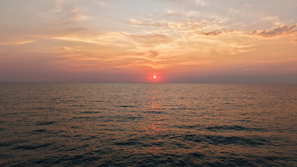 Gentle waves rolling onto the shore during a vibrant sunset, painting the ocean with warm hues of orange and pink, creating a serene and picturesque scene