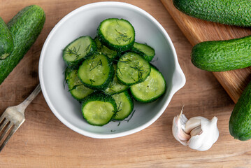 Organic cucumbers slices in a ceramic white bowl on a wooden table.