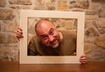 Male in frame head shoulders bearded intense stare eyes tilted sideways against stone wall...
