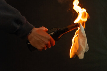 A hand holding a bottle with a burning rag against a dark background - symbolic of street protest or conflict.