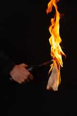 Close-up of burning bottle in hand on black background,