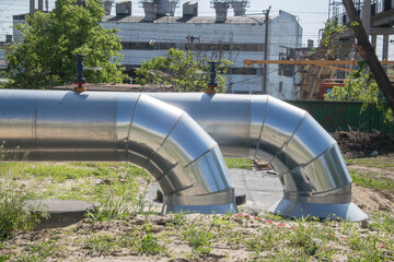 two large shiny water pipes with metal vents. In the background is a large old industrial building of the city boiler house