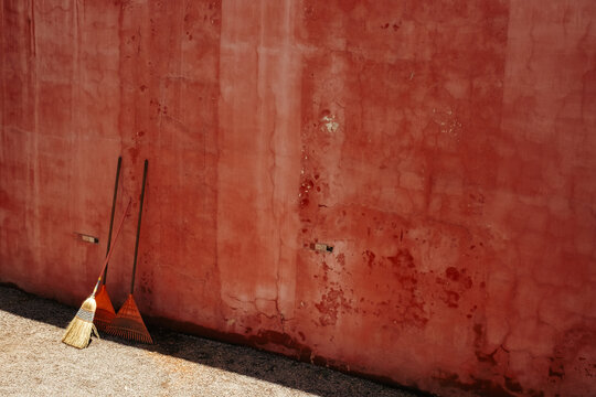 Rustic Brooms Leaning Against a Weathered Red Wall in Mexico City