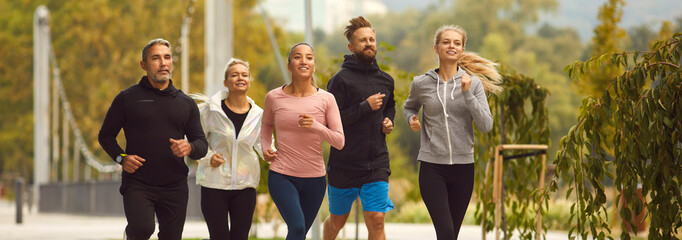 Team of young people men and women running together in the park having sport workout outdoors. Group of runners training in nature jogging in city park. Healthy lifestyle and fitness concept. Banner.
