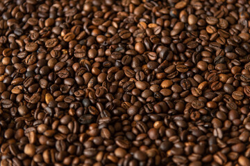 Dark roasted coffee beans are spread out on surface, showcasing their rich brown color and textured background. This display highlights the quality and variety of arabica or robusta beans. Copy space.