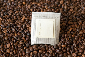 Close-up view of closed white blank paper drip coffee bag with ground arabica lying over roasted...