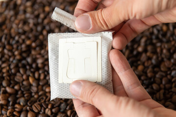 Close-up view of male person's hands opening white paper drip coffee bag with ground arabica over...