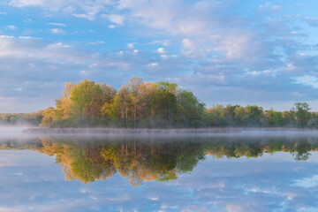 Landscape at sunrise of the foggy, spring shoreline of Whitford Lake with reflections in calm water, Fort Custer State Park, Michigan, USA