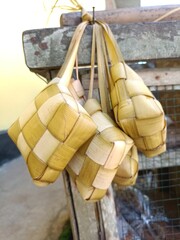 Traditional woven coconut leaf rice containers (Ketupat) hanging on a wooden surface, commonly used during Eid celebrations in Southeast Asia.
