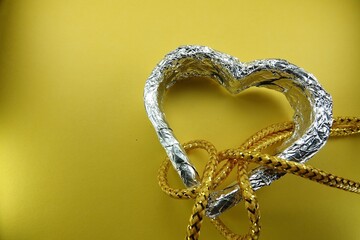 Srebrne serce na żółtym tle, przeplecione żółtymi sznurkami