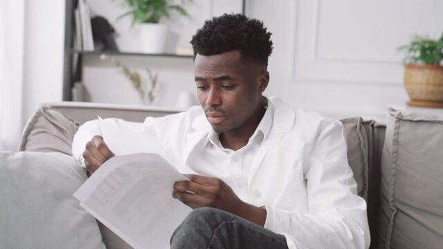 Portrait of virologist viewing medical records and feeling tiredness, black man. Medical student sitting alone in clinic office, intern studying in modern hospital, health professional working