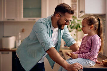 Fototapeta premium Smiling little girl talking to her father in kitchen.