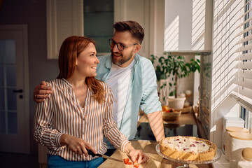 Happy couple talking while making cake in kitchen.