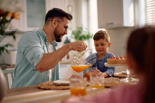 Happy father pouring fresh juice to his son at dining table.