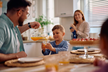 Happy father and son having glass of orange juice during family desert at dining table.