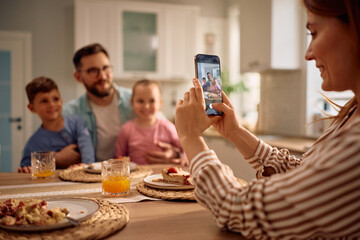Close up of woman taking picture of her family at dining table.