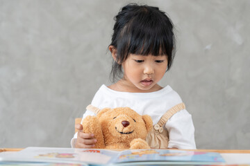 Happy Asian children relax read story book for bear doll. daughter and reading a story. learn development, childcare, education, storytelling, practice, imagine, reduce addiction mobile phone