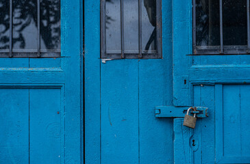 Puerta antigua de madera azul con cerradura oxidada y ventanas con barrotes