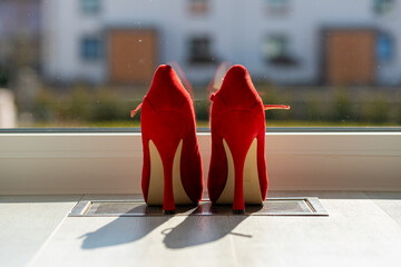Red ladies pumps on the floor in front of a window