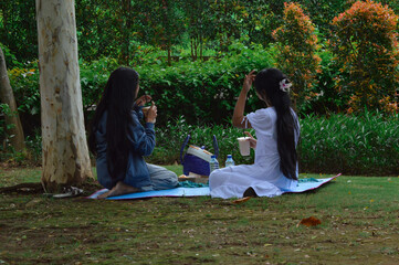 Sitting peacefully on a mat, the girls sip their drinks under the trees, savoring the tranquility...