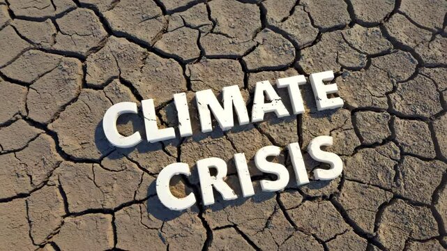 High angle shot of weathered white Climate Crisis text on a parched and cracked mudflat under sunlight