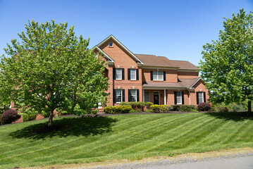 Large, beautiful, single-family brick country house. Large lawn and green trees.