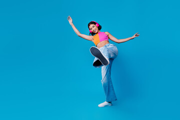 Cheerful young woman wearing headphones dancing against a bright blue background with vibrant style...