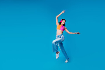 Young stylish woman in bright outfit dancing with headphones against blue background showcasing vibrant lifestyle