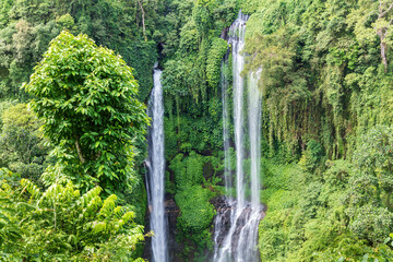Triple waterfall at Sekumpul waterfall, northern Bali, Indonesia. Water cascading down steep cliffs, covered in lush jungle vegetation.
