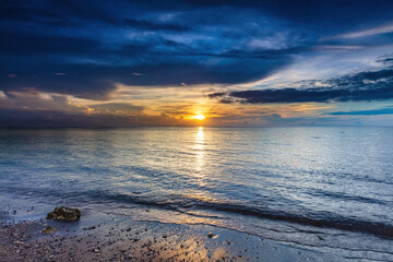Ocean sunset at Lovina Beach, northern Bali, Indonesia. Beach in foreground; setting sun surrounded by colorful clouds. Sun's reflection on the water. 
