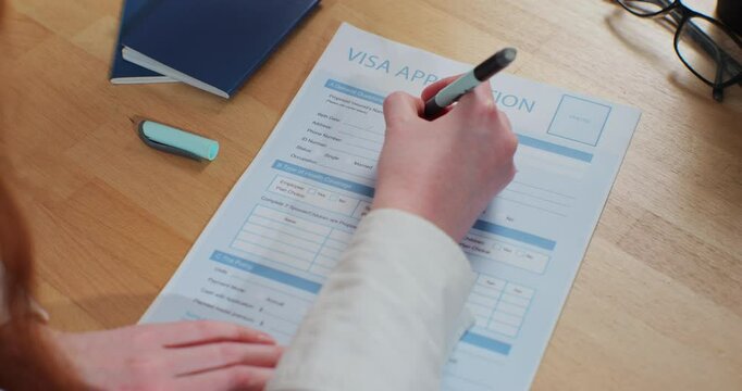 Woman hand filling visa application form on desk. Legal immigration, tourist interview.