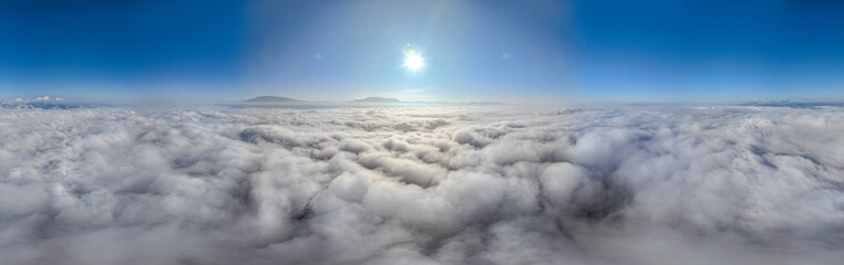 A serene view of the early morning sun rising above a vast sea of clouds, with distant mountain peaks faintly visible on the horizon, creating a peaceful and ethereal landscape. Flying over the cloud
