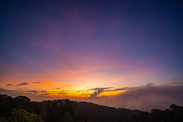 stunning mountainous landscape at sunrise with vibrant orange and pink hues illuminating the clouds against a blue sky. layer of mist settled in the valley, giving the scene a dreamy.
