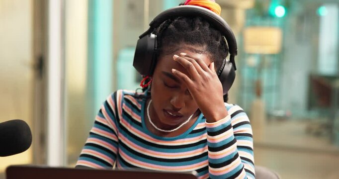 Black woman, headache and headphones with podcast, stress and exhausted with fatigue on live stream. African influencer, girl and mic with migraine, pain or burnout with brain fog by laptop in studio