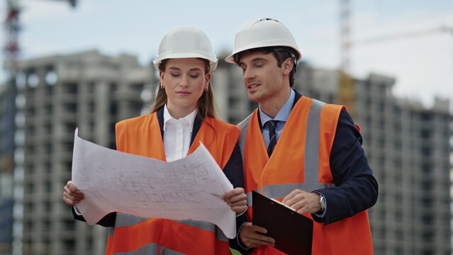 Two engineers examine blueprints discussing project at construction site closeup