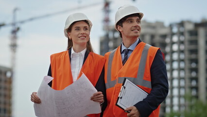 Smiling builders review construction plans at outdoor building site closeup.