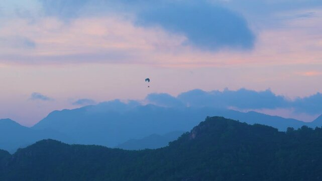 Paragliding sport twilight casts a stunning glow over the mountains as soft clouds float in the pastel sky, creating a peaceful atmosphere in the landscape at dusk