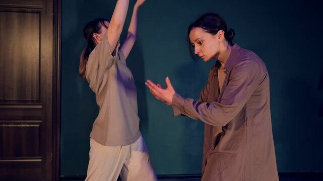 Two female dancers are rehearsing modern choreography improvisation in the studio. Couple of Caucasian ballet artists in casual clothes are moving in duet performing sensitive contemporary cooperation