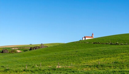 Fototapeta premium Tranquil landscape of undulating green hills with a solitary white and red church