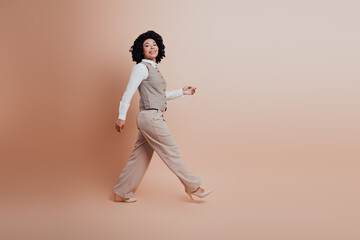 Confident young businesswoman walking in elegant beige formalwear against a beige studio background
