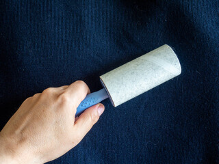Clothes cleaning from pet hair, dust and debris. Hand holds sticky lint roller. Quickly and easily remove pet hair, dander, dust, lint and allergens from furniture, clothing and household surfaces