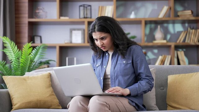 Disappointed young woman complains about poor performance of program on laptop sitting on sofa in living room at home. Frustrated upset female is dissatisfied with work of computer Internet or service