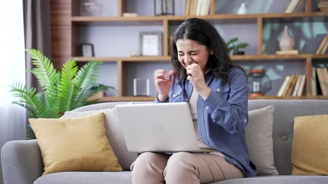 Satisfied happy young woman reading great news on laptop while sitting on sofa in living room at home. Smiling glad female freelancer received positive good message on computer, celebrating success