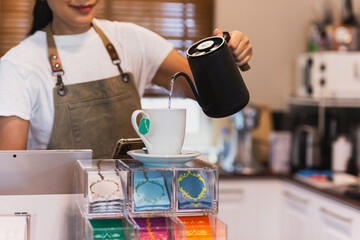 Woman with apron pouring hot water into a mug make herbal tea.