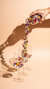 Wildflowers cascading from a bottle into wine glasses on a beige background.