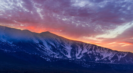 highland mountain landscape of beautiful sunset or sunrise behind nice mountain peaks and slopes in snow and majestic cloudy sky on background