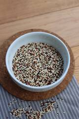 Close-up of mix of raw black, red and white quinoa seeds in a ceramic bowl on wooden table