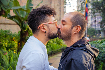 Fototapeta premium Mature bald man couple and young curly haired gay geek showing their love outdoors at sunset for love, diversity, pride, freedom and happiness concept. High quality photo